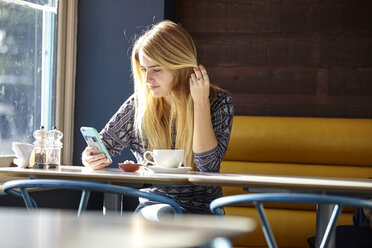 Young woman alone in cafe reading smartphone texts - CUF13353