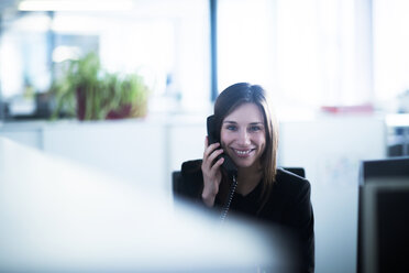 Young woman in office using telephone looking at camera smiling - CUF13371