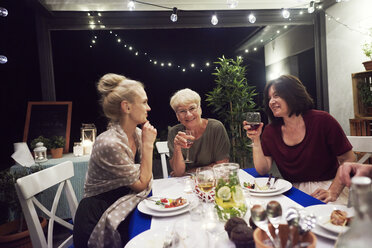 Drei Frauen sitzen am Esstisch und trinken aus Weingläsern - ISF06212