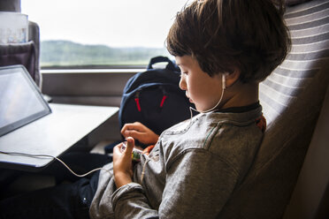 Junge, der im Zug reist und ein digitales Tablet benutzt und Kopfhörer trägt - ISF06214