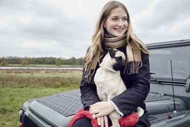 Junge Frau sitzt auf einem Geländewagen in einem Feld mit einem Hund auf dem Schoß - ISF06244