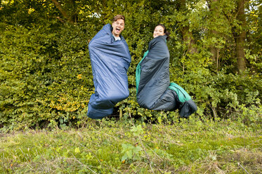 Junges Paar springt in ihren Schlafsäcken durch die Luft - CUF13395