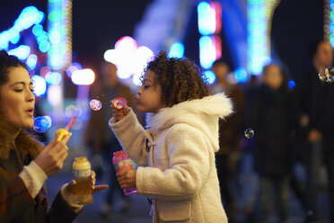 Mother and daughter blowing bubbles, at funfair - CUF13405