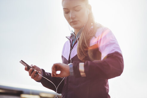 Mittlere erwachsene Läuferin mit Kopfhörern, die die Zeit auf ihrer Smartwatch überprüft - CUF13415