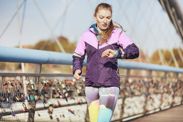 Mittlere erwachsene Läuferin, die beim Laufen über eine Brücke die Zeit kontrolliert - CUF13416