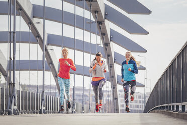 Three female runners running on city footbridge - CUF13417