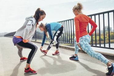 Three female runners doing warm up exercise on footbridge - CUF13426