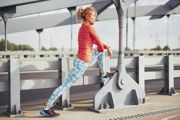 Young female runner warming up on city footbridge - CUF13440