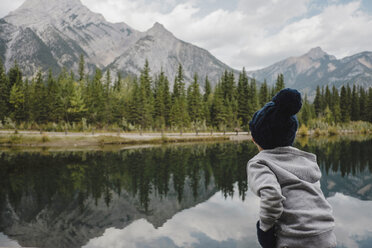 Boy looking at reflection of mountain and trees in lake, Canmore, Canada, North America - ISF06328