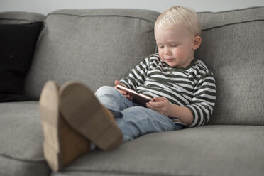 Young boy sitting on sofa, looking at smartphone - ISF06349