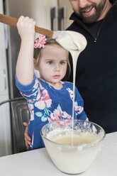 Mädchen mit Vater starrt auf Holzlöffel Nieselregen an Küchentisch - ISF06376