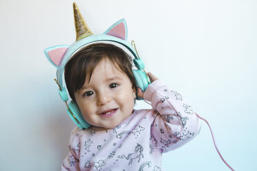 Porträt eines lächelnden kleinen Mädchens mit Einhorn-Kopfhörern beim Musikhören - GEMF02009
