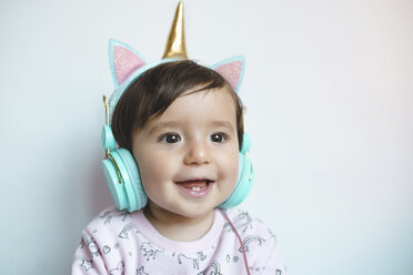 Porträt eines lächelnden kleinen Mädchens mit Einhorn-Kopfhörern beim Musikhören - GEMF02012