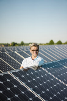 Lächelnder reifer Mann mit Sonnenbrille lehnt sich an ein Solarpanel - MOEF01128