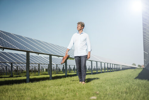 Mature man walking barefoot on meadow between solar panels - MOEF01137