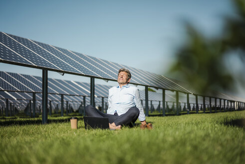 Älterer Mann sitzt barfuß auf einer Wiese, Laptop und Coffee-to-go-Becher, Solaranlage - MOEF01144