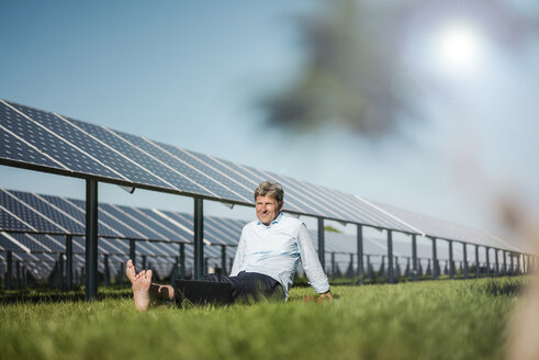 Älterer Mann sitzt barfuß auf einer Wiese, Solaranlage - MOEF01145