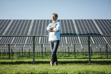 Älterer Mann mit Laptop steht barfuß auf einer Wiese, Solaranlage - MOEF01148