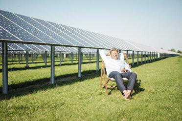 Lächelnder reifer Mann im Liegestuhl sitzend, Solaranlage - MOEF01150