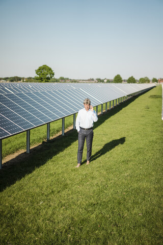 Geschäftsmann benutzt Smartphone im Solarpark, lizenzfreies Stockfoto