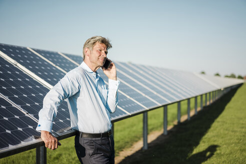 Businessman using smartphone at solar park - MOEF01172