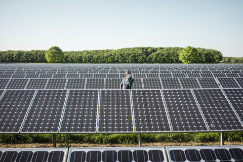 Älterer Mann, der ein Smartphone benutzt und auf einem Panel in einer Solaranlage steht, lizenzfreies Stockfoto