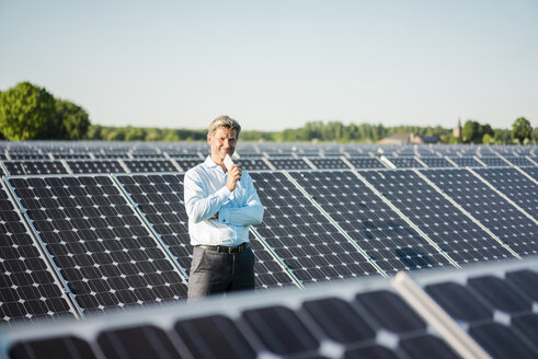 Mature man with smartphone standing in solar plant - MOEF01184