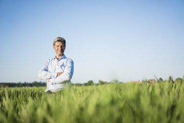 Businessman standing in grain field, arms crossed - MOEF01195