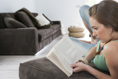 Junge Frau, die auf dem Sofa liegt und ein Buch liest - CUF13690