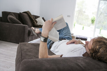 Junger Mann, der auf dem Sofa liegt und ein Buch liest - CUF13691