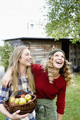 Zwei Frauen im Garten mit Korb voller Äpfel, lachend - CUF13760