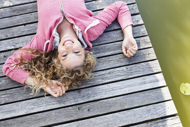 Junge Frau liegt auf einer Holzterrasse und lächelt in die Kamera - CUF13768