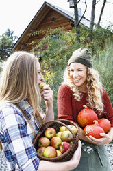 Two friends carrying homegrown produce, one woman eating apple - CUF13785