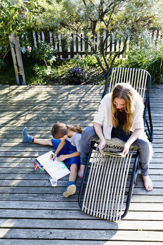 Mutter mit Tablet, Tochter malt auf einer Holzterrasse, lizenzfreies Stockfoto