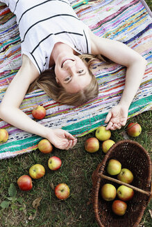 Woman lying on striped rug with basket of apples - CUF13795