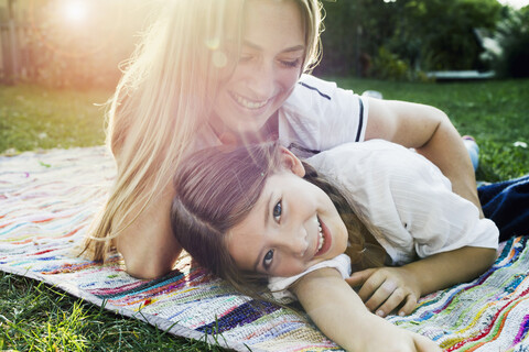 Mutter und Tochter liegen auf einem Teppich im Garten, lizenzfreies Stockfoto