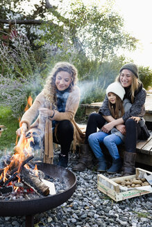 Zwei Frauen und ein Mädchen sitzen an einer Feuerstelle und entspannen sich - CUF13804