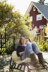 Mittlere erwachsene Frau entspannt sich auf einem Liegestuhl auf einer Holzterrasse - CUF13832