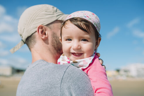 Porträt eines glücklichen kleinen Mädchens in den Armen des Vaters am Strand - GEMF02016