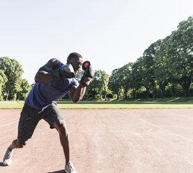 Junger afroamerikanischer Mann trainiert Boxen auf einem Sportplatz, im Freien - UUF13869