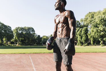 Young Afro-American man training boxing on sports field, outdoors - UUF13872