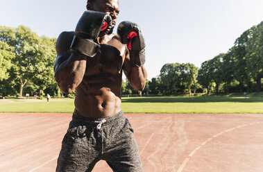 Young Afro-American man training boxing on sports field, outdoors - UUF13874