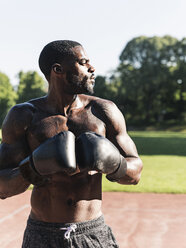 Young Afro-American man training boxing on sports field, outdoors - UUF13875