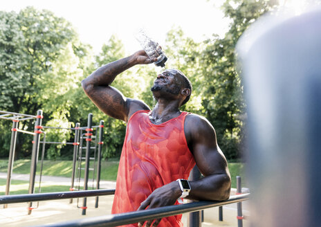 Young athlete training on parallel bars, outdoors, pouring water over in his face - UUF13887