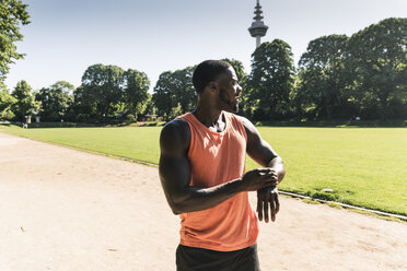 Young athlete in training on sports field taking the time on his smartwatch - UUF13891