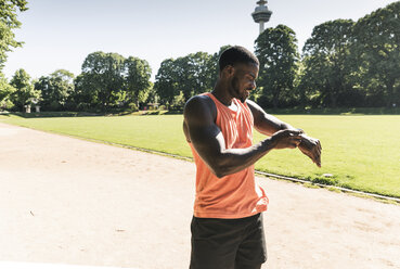 Junger Sportler beim Training auf dem Sportplatz, der die Zeit auf seiner Smartwatch misst - UUF13893