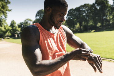 Junger Sportler beim Training auf dem Sportplatz, der die Zeit auf seiner Smartwatch misst - UUF13894