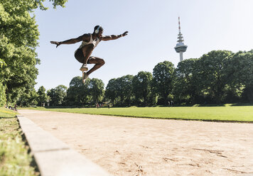 Junger Sportler mit Kopfhörern, der Musik hört, beim Weitsprungtraining - UUF13904