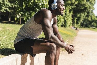 Smiling young athlete taking a break, wearing headphones, listening music - UUF13906