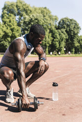 Young athlete doing weight training with dumbbells on sports field - UUF13907